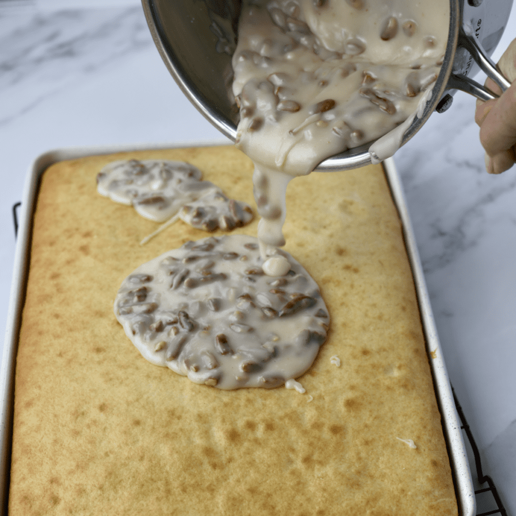 Pouring Butter Pecan Icing on a vanilla sheet cake.
