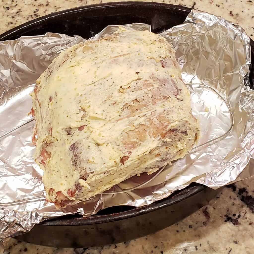 Standing beef rib roast covered in butter on a rack in a baking pan.
