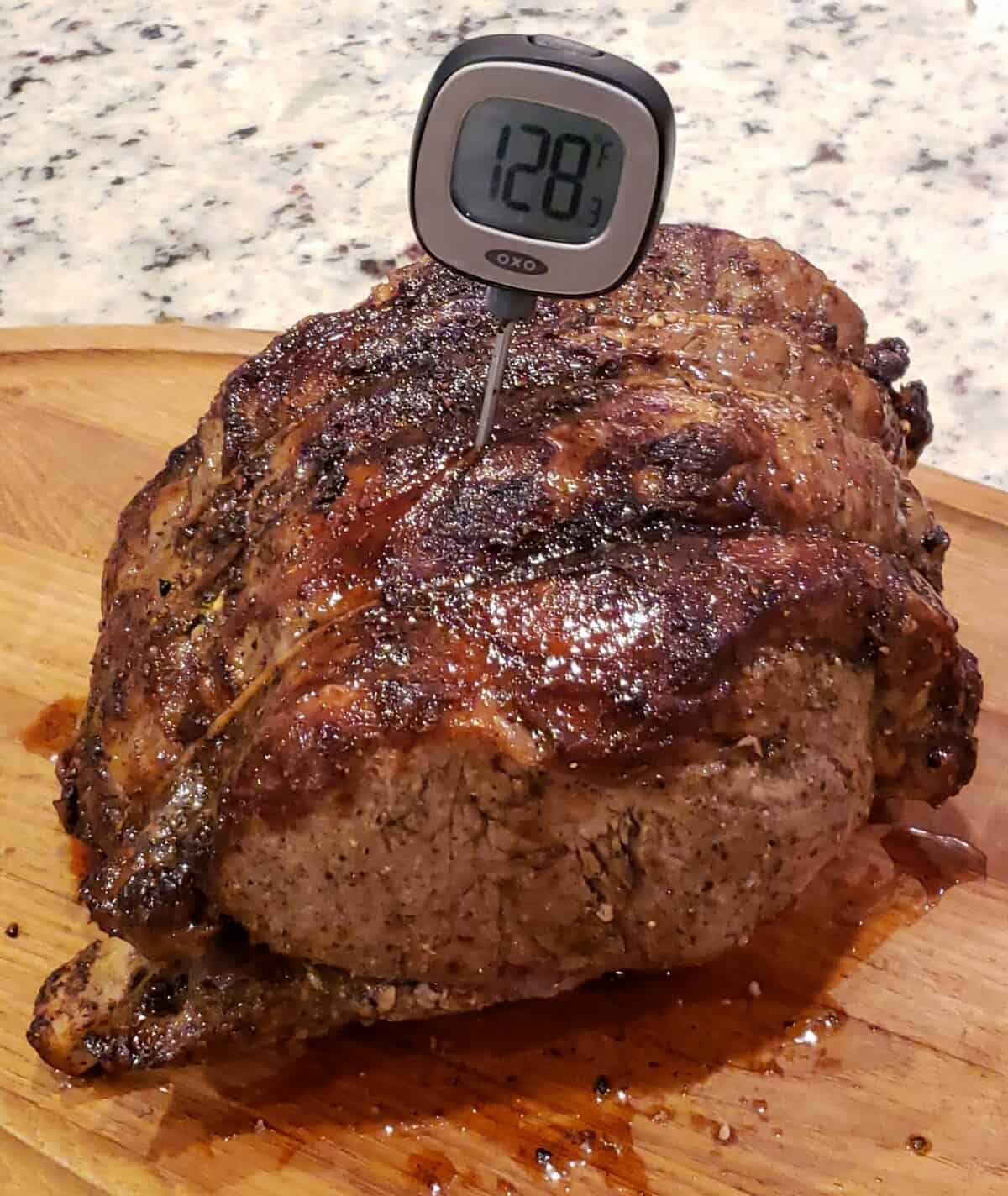 Bone in cooked standing rib roast with meat thermometer stuck in the top.