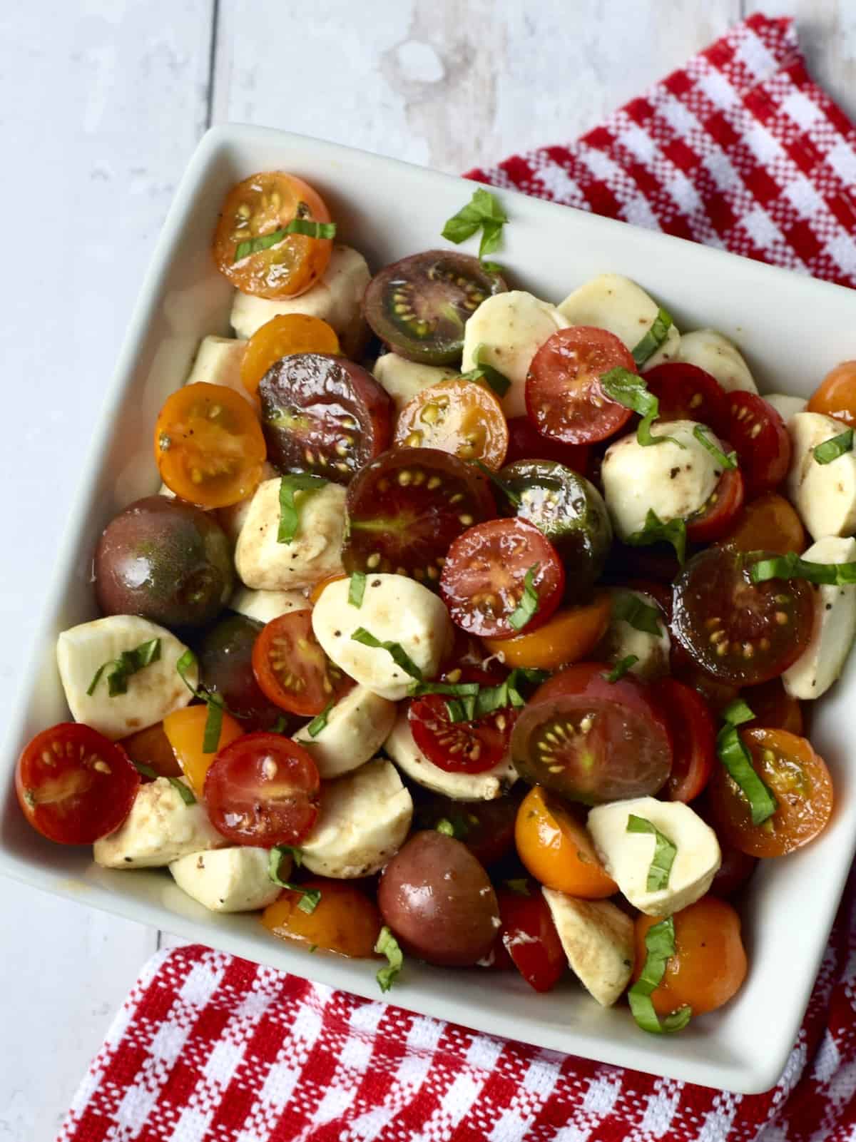 White bowl filled with dressed salad of cherry tomatoes, cubes of mozzarella cheese and shredded basil leaves.