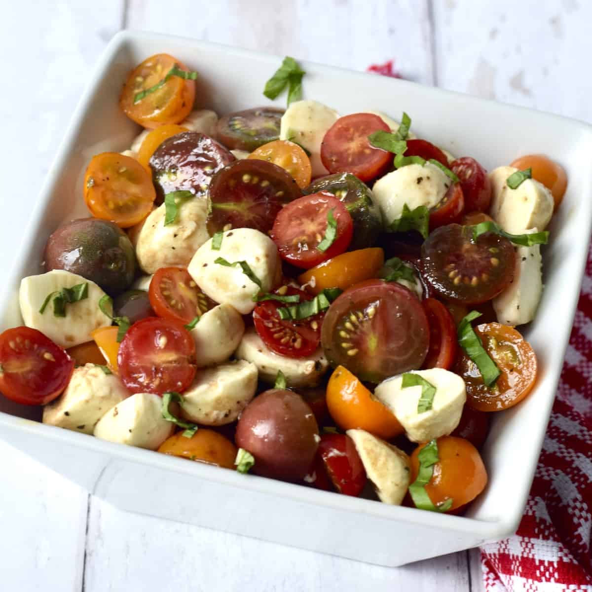 White bowl filled with dressed salad of cherry tomatoes, cubes of mozzarella cheese and shredded basil leaves.