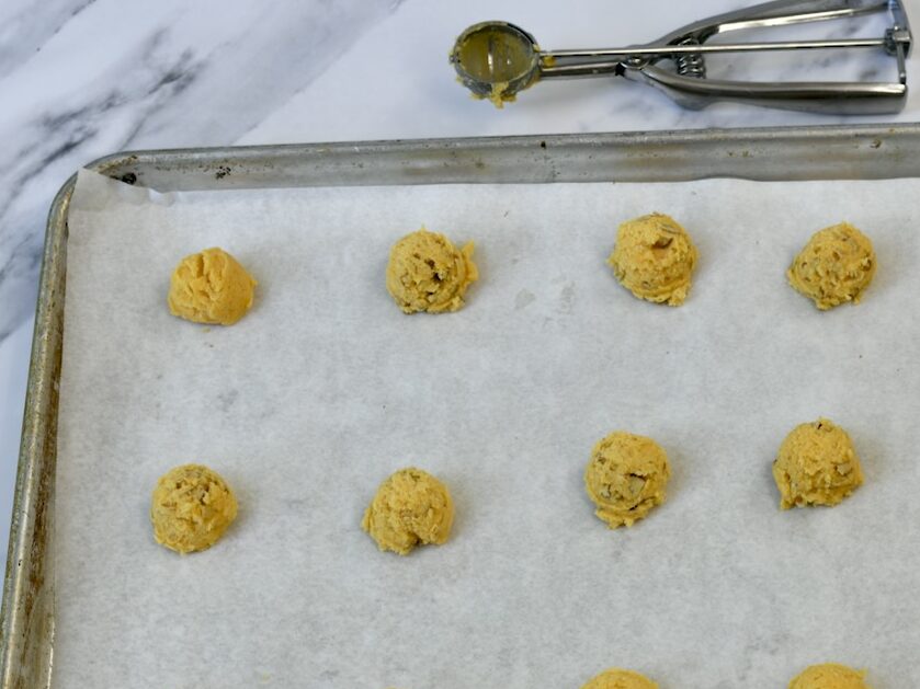 Scooped balls of cheese wafers lined up on a parchment paper covered cookie sheet.
