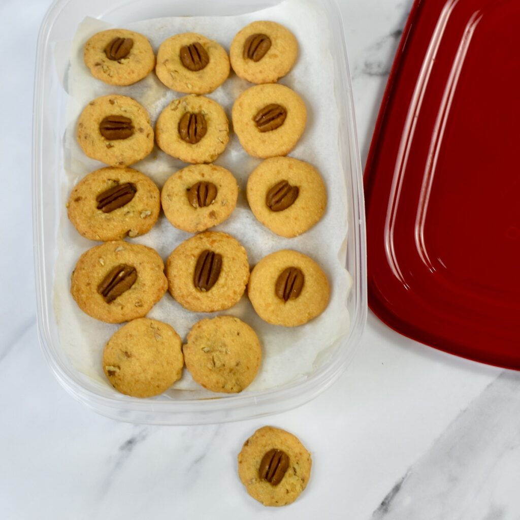 Baked pecan cheese wafers placed in airtight container for freezer storage.