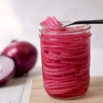 open jar of pickled red onions with a fork set on top of jar scooping out some pickles.