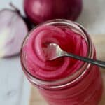 an open jar of pickled red onions with a portion of onion on a fork