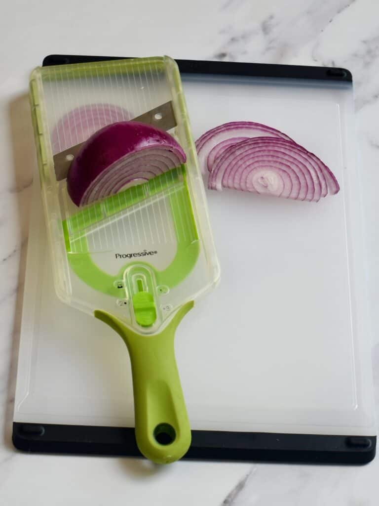 a hand held mandolin set on a board with sliced red onion
