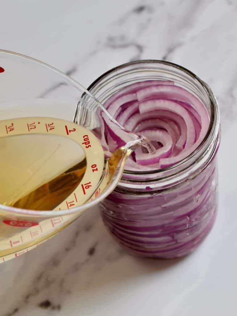 a jar of sliced red onions with a pickling liquid being poured over