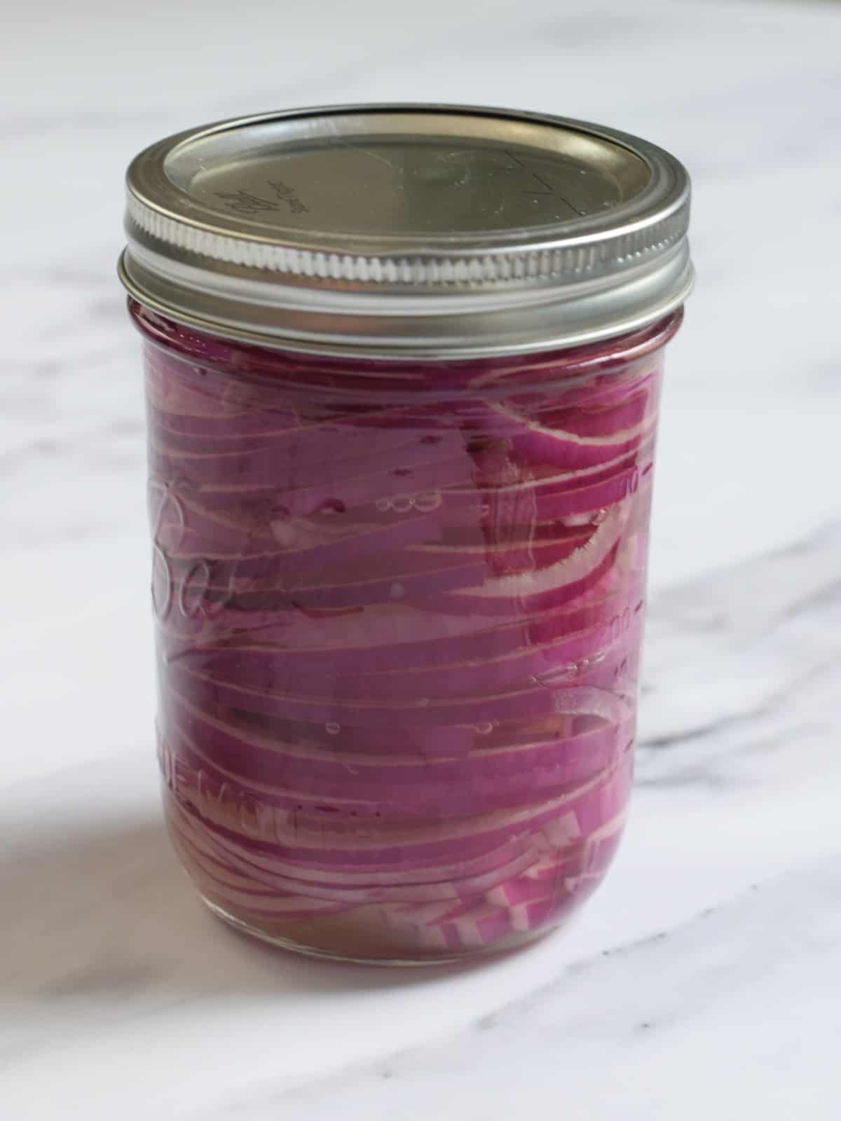a Mason jar filled with pickled red onions with lid on.