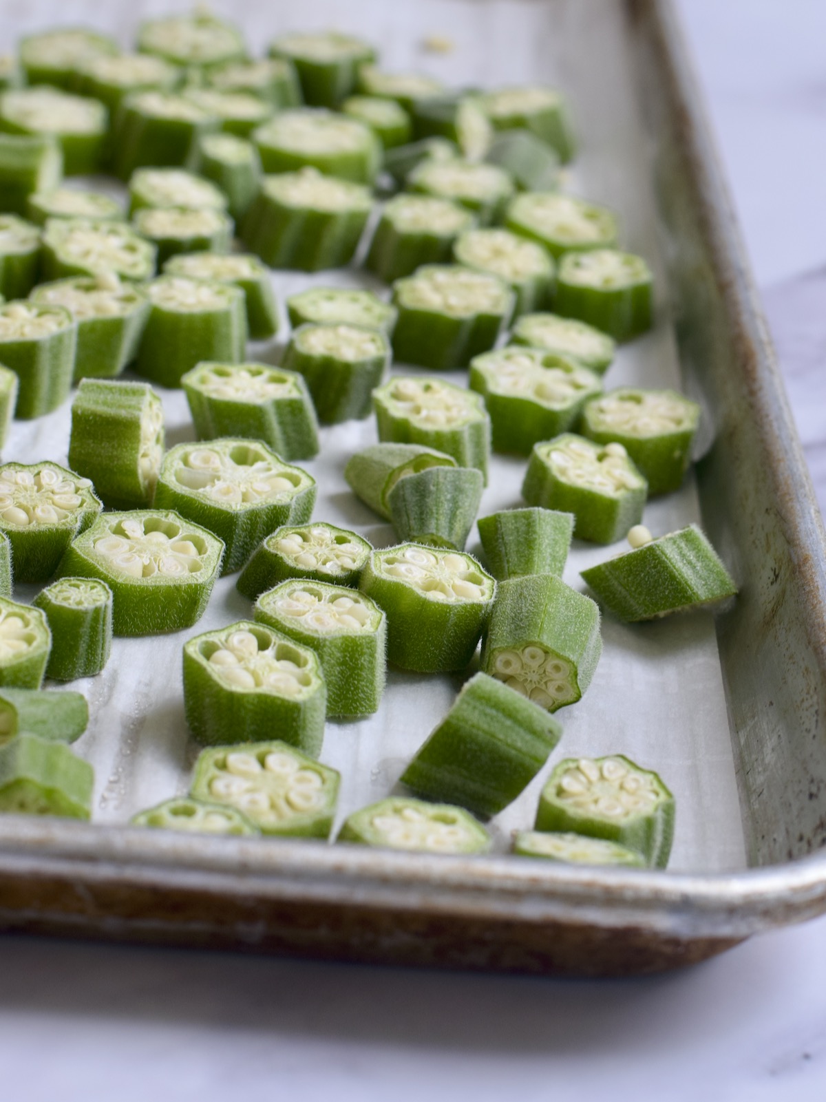 A lined baking sheet filled with slices of frozen okra.