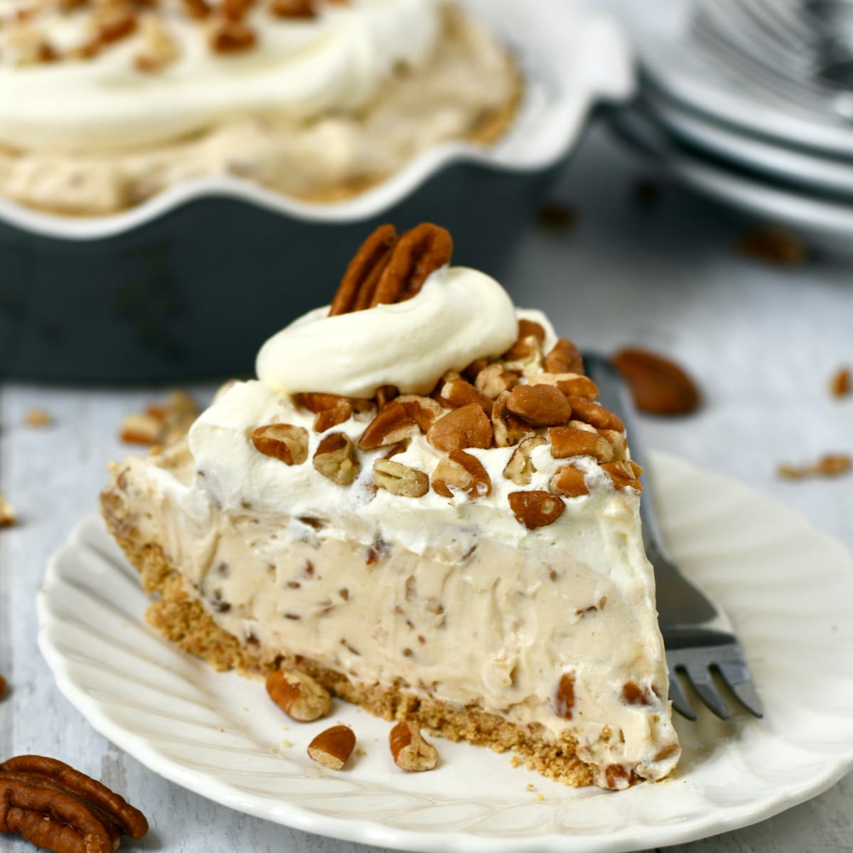 Slice of pecan cream pie on white plate in front of whole pie in background.