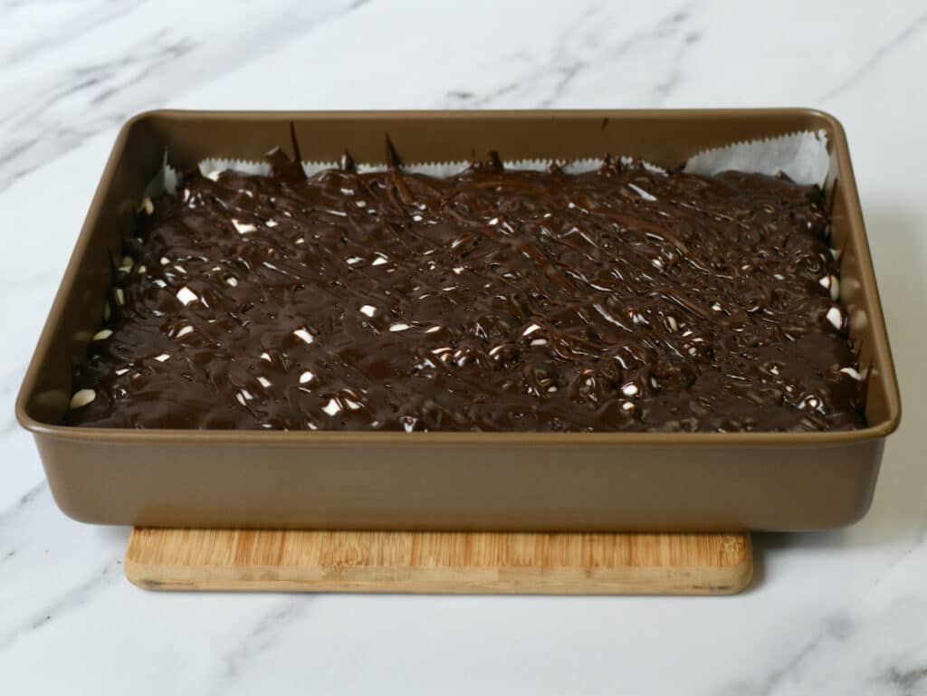 Chocolate iced marshmallow brownies in the pan on top of wooden cutting board.