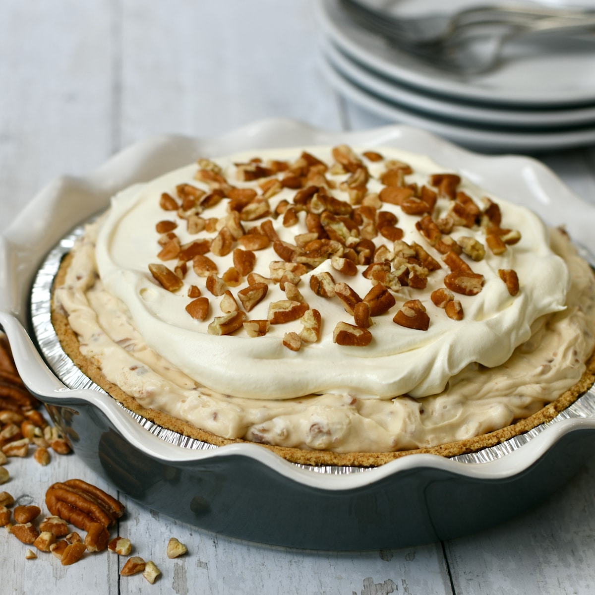Pecan cream pie with graham cracker crust in a blue fluted pie plate and topped with pecans.