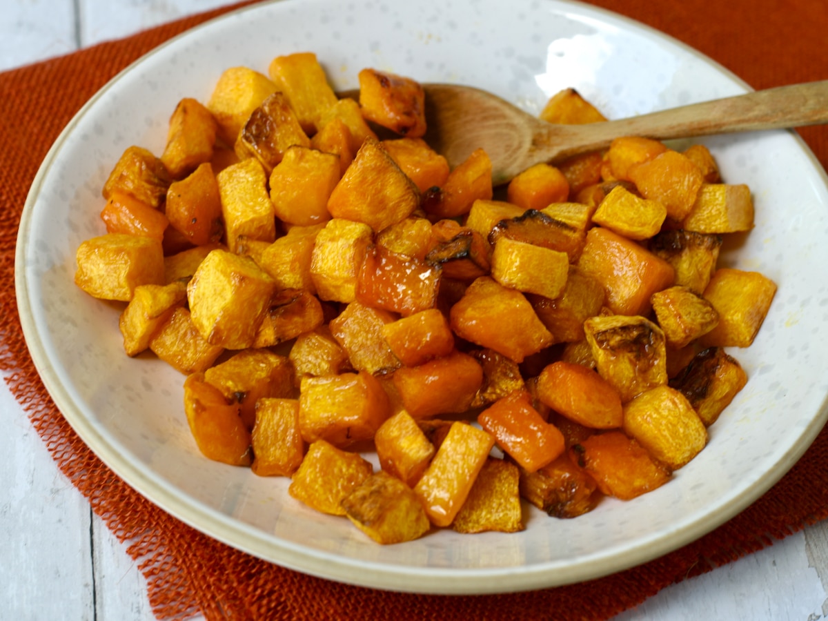 Bowl of roasted butternut squash on orange cloth with wooden spoon in bowl.