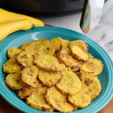 Air fryer fried yellow squash on blue plate with air fryer in background.