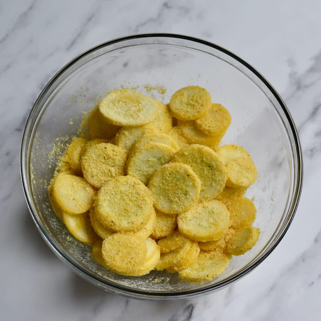 Sliced yellow squash tossed in a bowl of yellow cornmeal.
