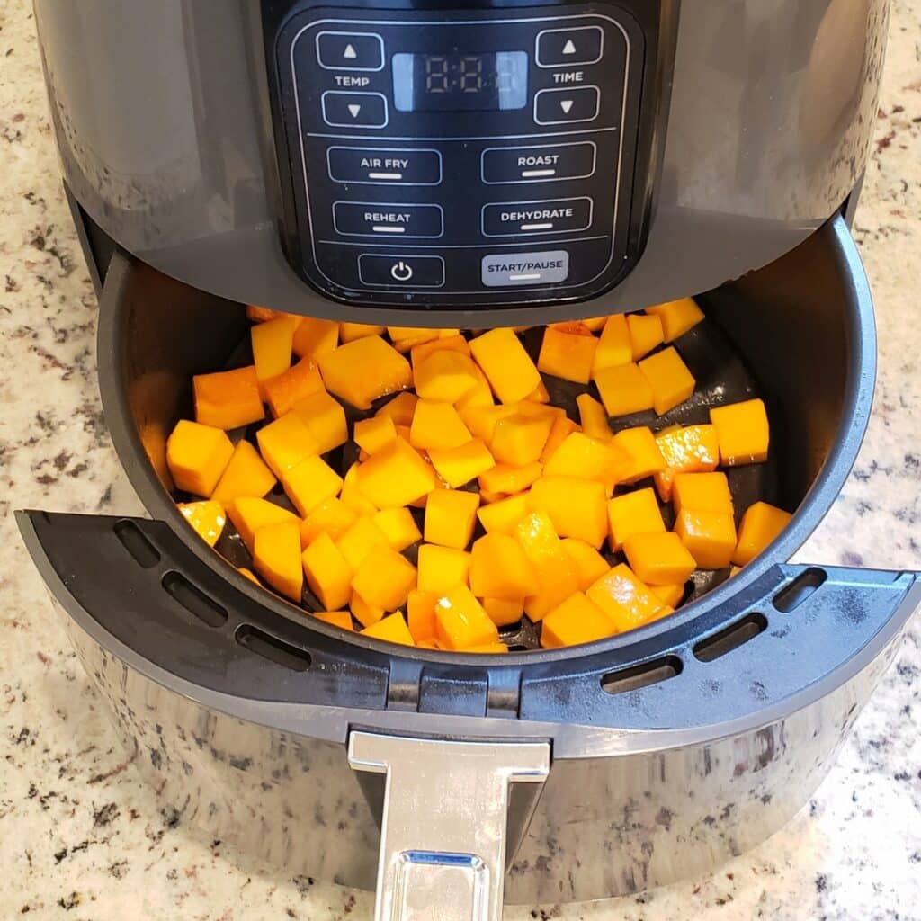 An air fryer basket filled with cubes of butternut squash coated in oil.