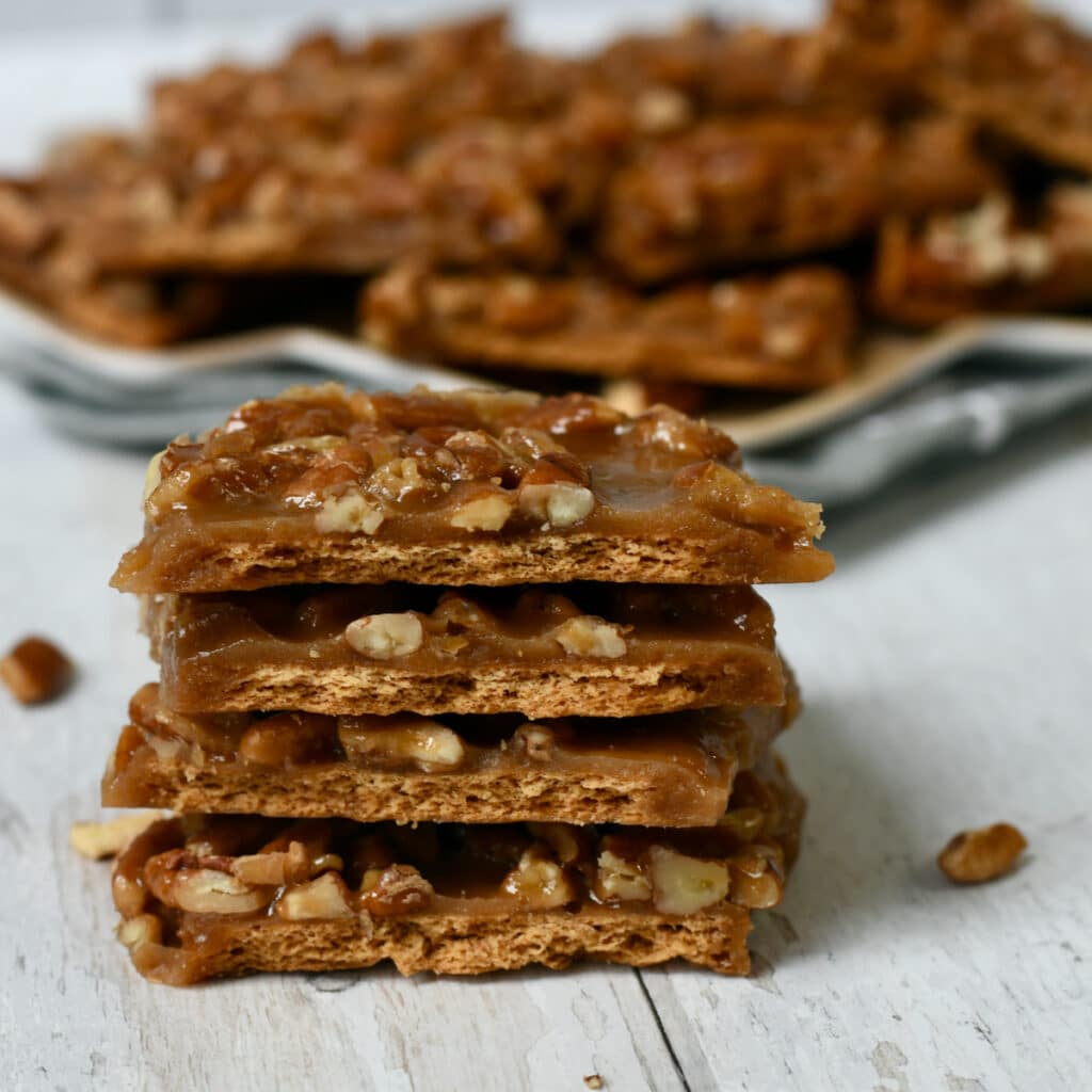 Pecan Pie Bark Candy stacked with plate of bars behind them.