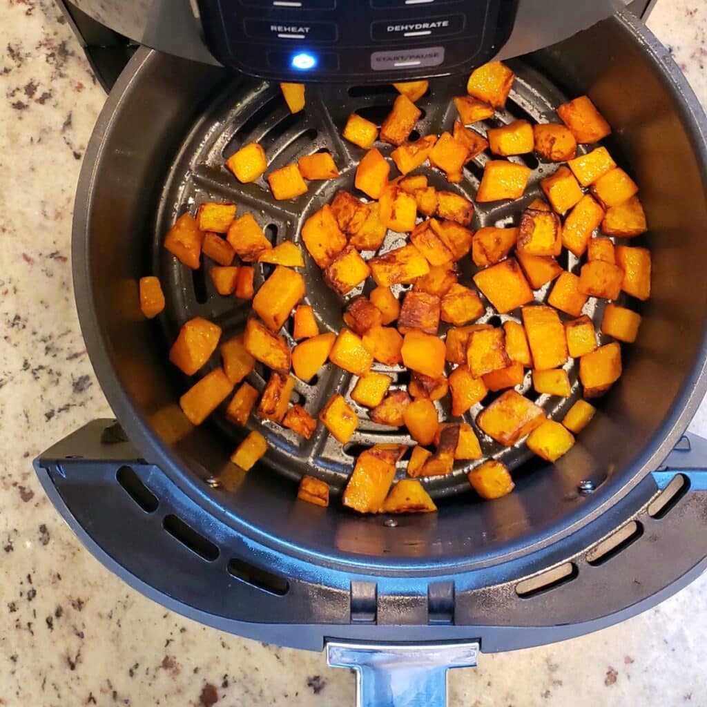 An air fryer basket filled with cubes of roasted butternut squash.