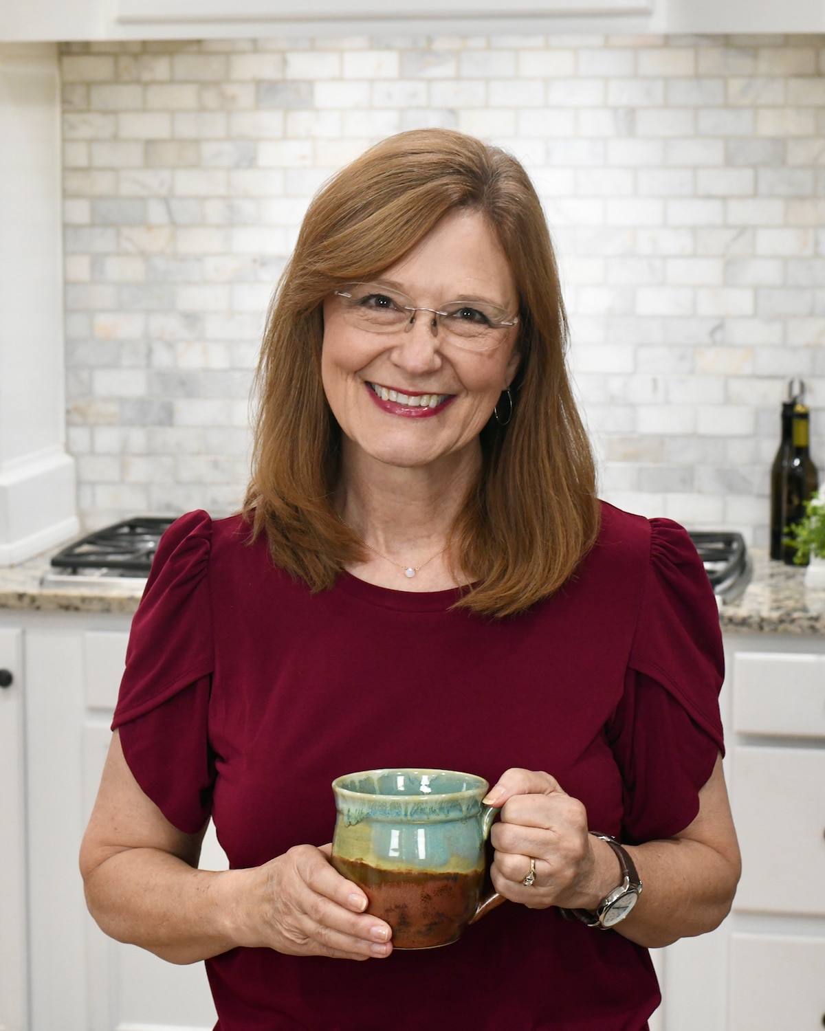 Woman in kitchen holding mug.