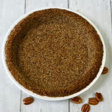 Pecan crust for pie with pecans scattered on the surface.
