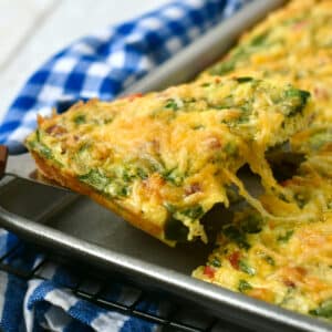 A square of sheet pan omelette being pulled from the pan with cheese pulling as its lifted.