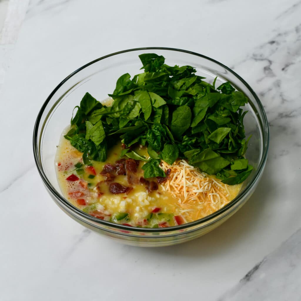 Spinach, cheese, eggs in a mixing bowl.
