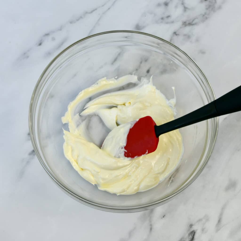 Combining cream cheese and mayonnaise in a glass bowl.