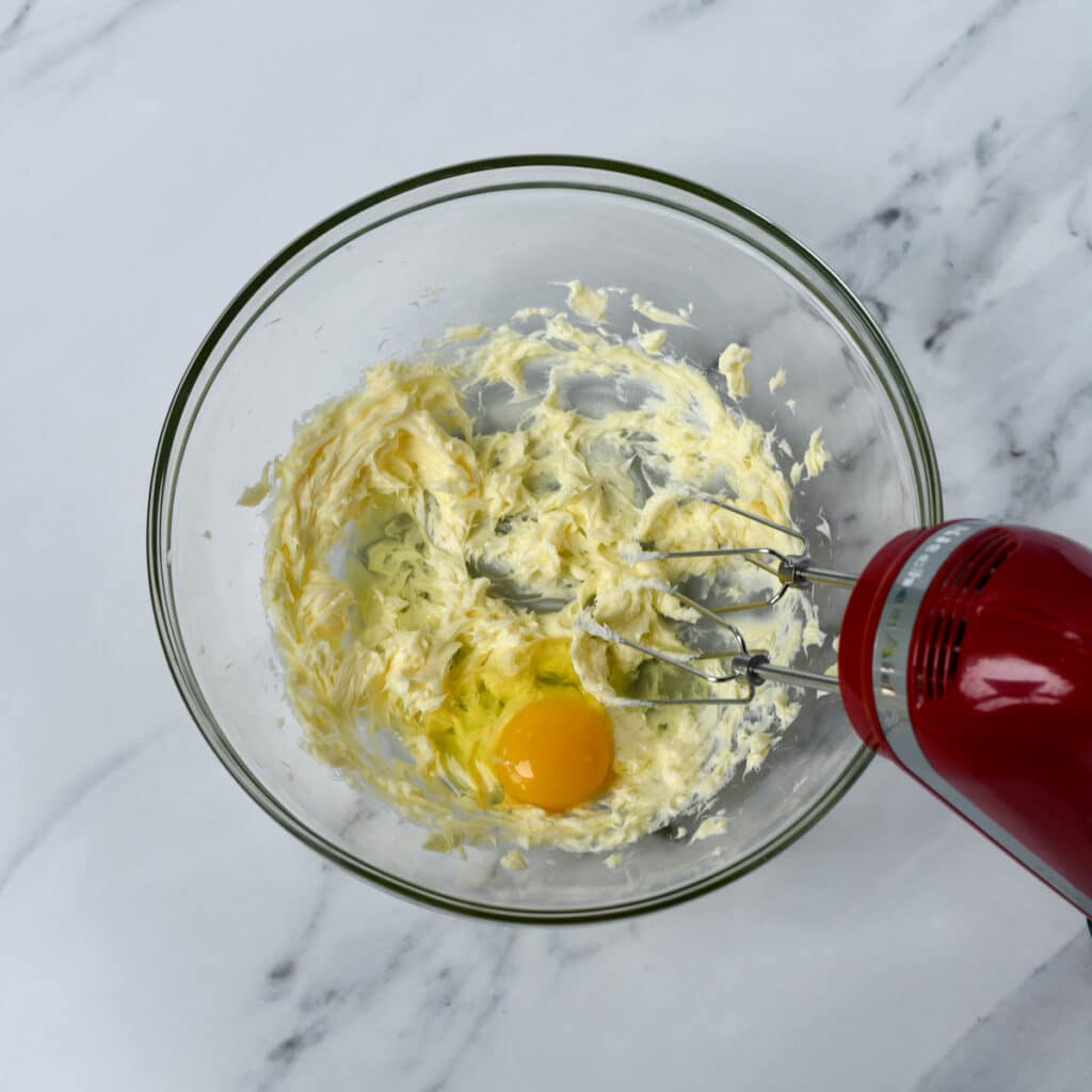 Using a hand mixer to beat egg into sugar and butter.