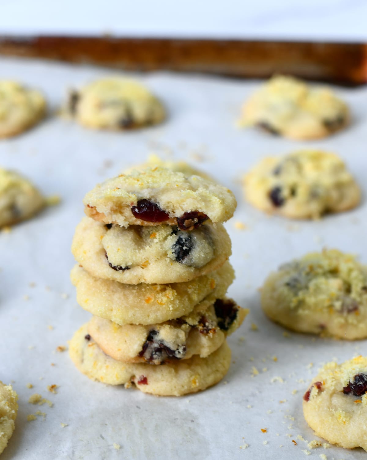 A stack of cranberry orange cookies on a baking sheet surrounded by more cookies.