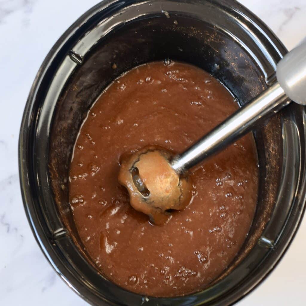Using an immersion blender to blend pear butter in a slow cooker.