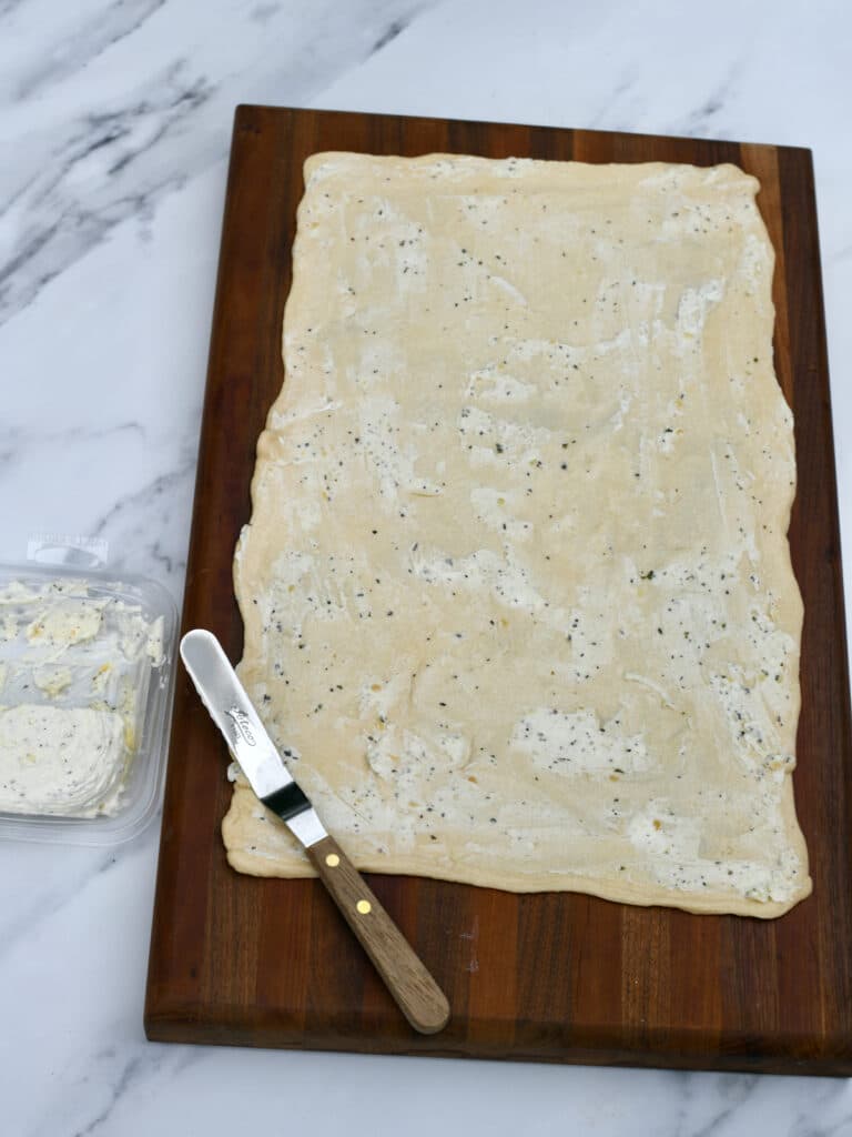 Crescent roll dough covered in garlic butter on wooden cutting board.
