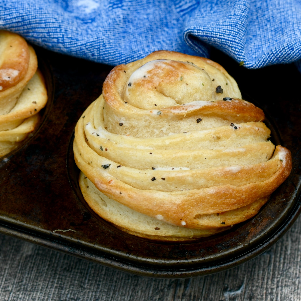 Baked garlic herb cruffins slathered in butter with blue cloth beside it.