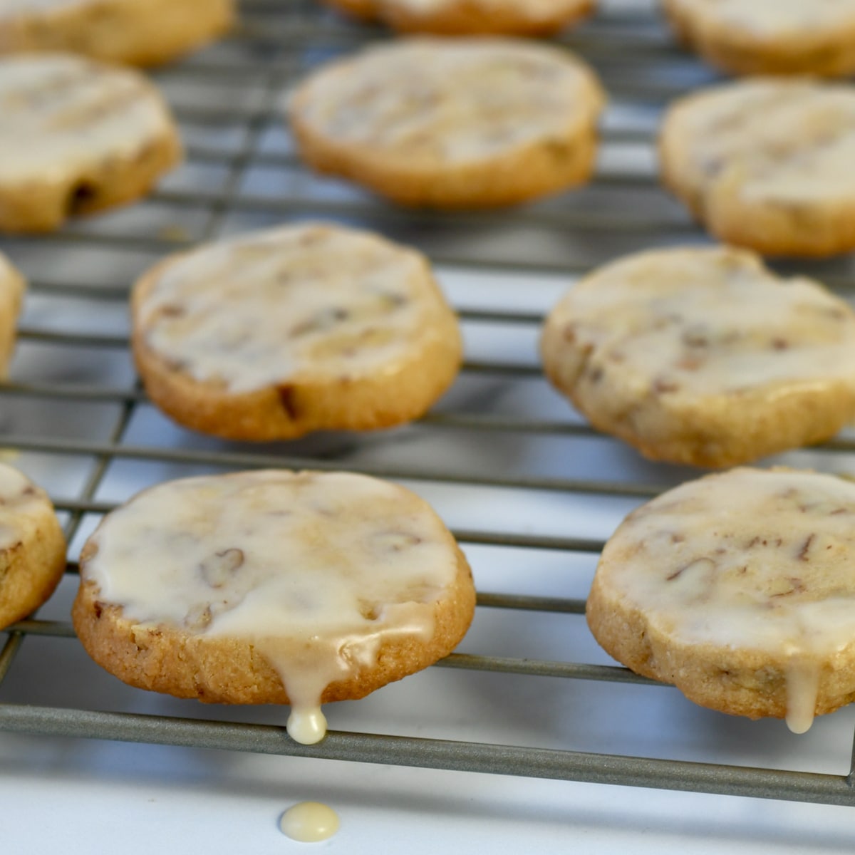 Maple glaze icing dripping off pecan shortbread cookie on wire rack.
