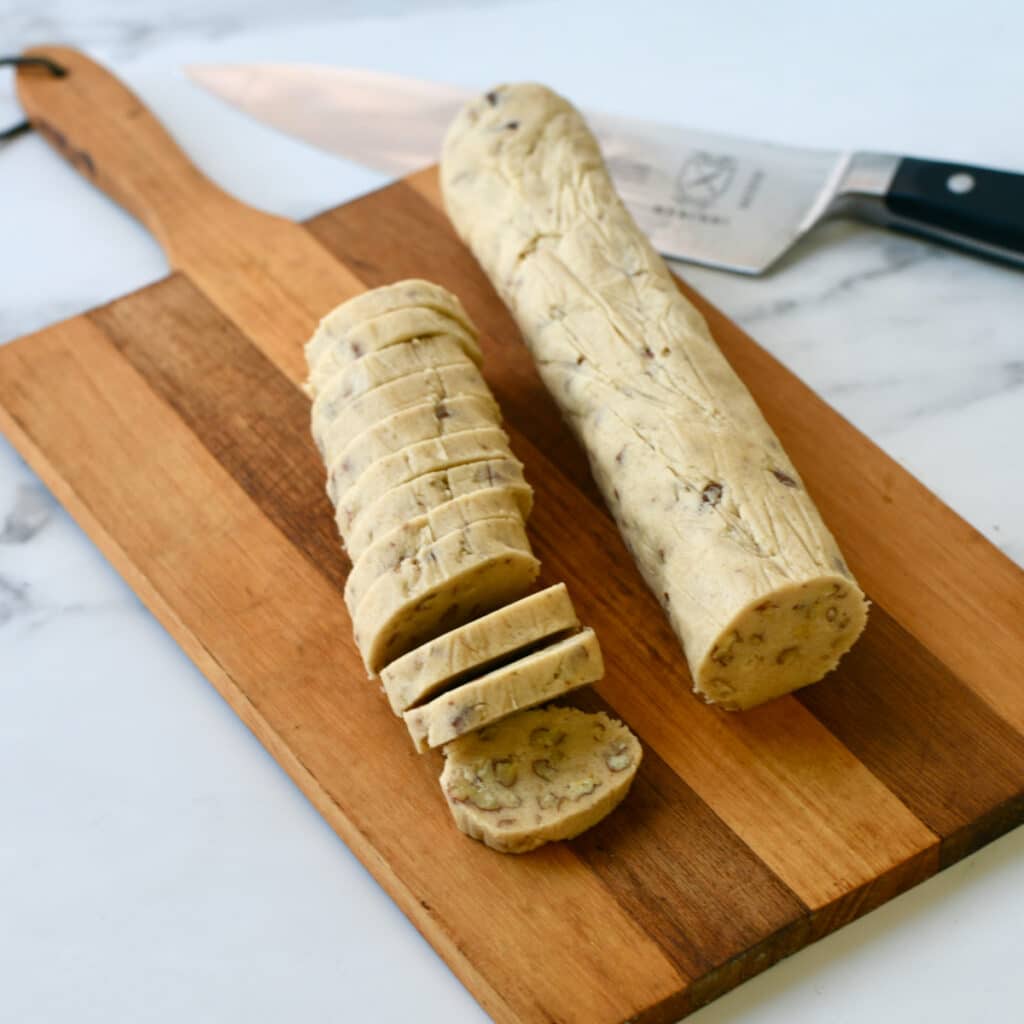 Maple pecan cookie dough rolls partially sliced on a wooden cutting board.
