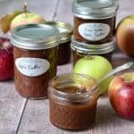 Several jars of slow cooker apple butter with whole apples scattered around.