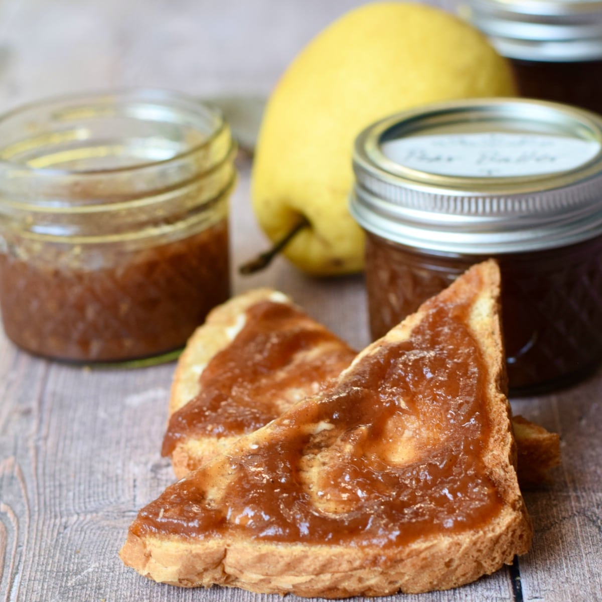 Square featured image of pear butter spread on triangular pieces of toast with two mason jars of pear butter in the background.