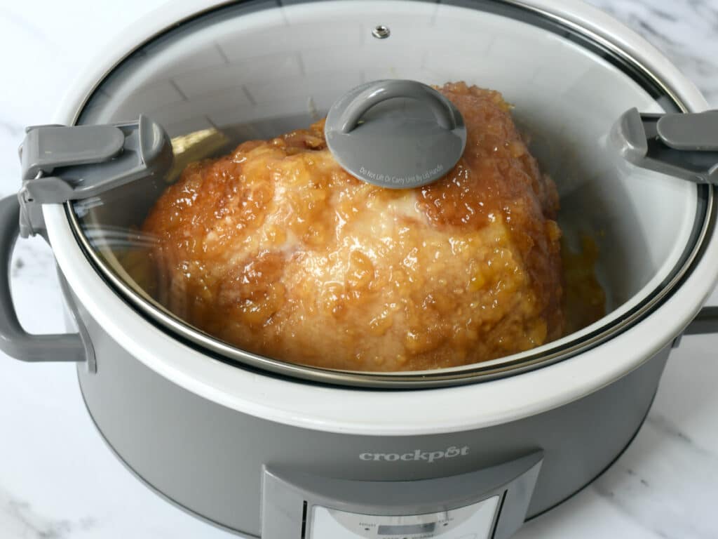 Adding the lid to the slow cooker to cook pineapple brown sugar ham.