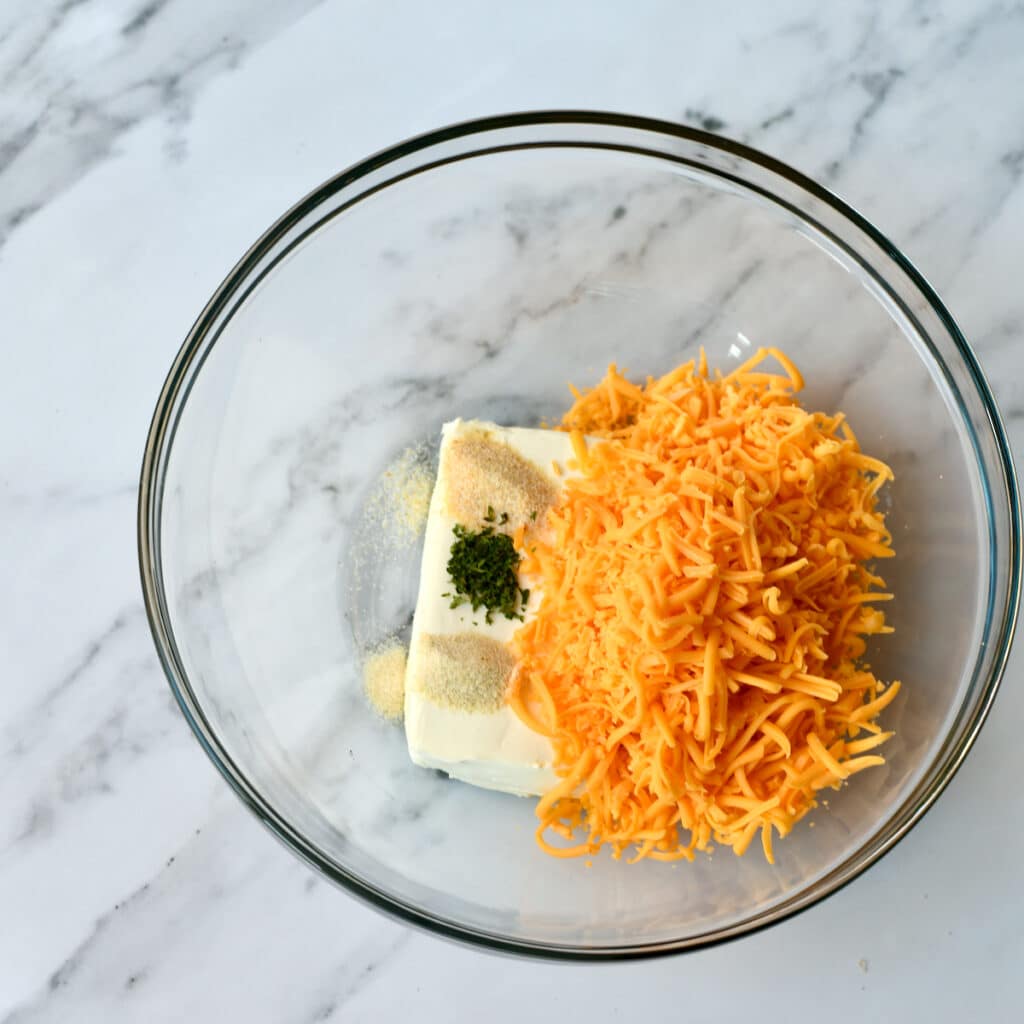 Cream cheese, cheddar and seasonings in a glass bowl.