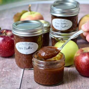 Spoonful of apple butter coming up out of a small Mason jar with apples in background.