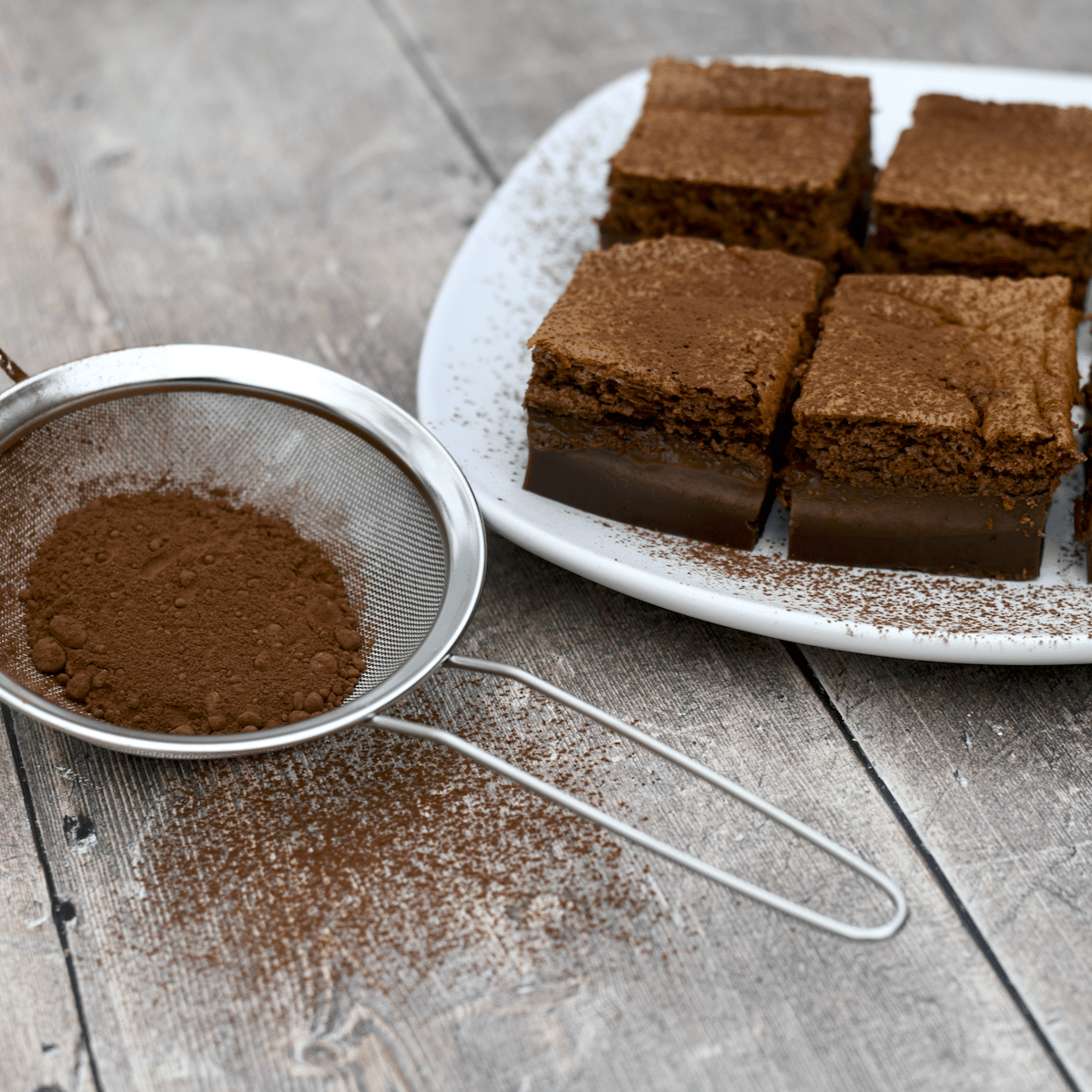 A plate of chocolate magic cake with a sifter filled with cocoa powder.