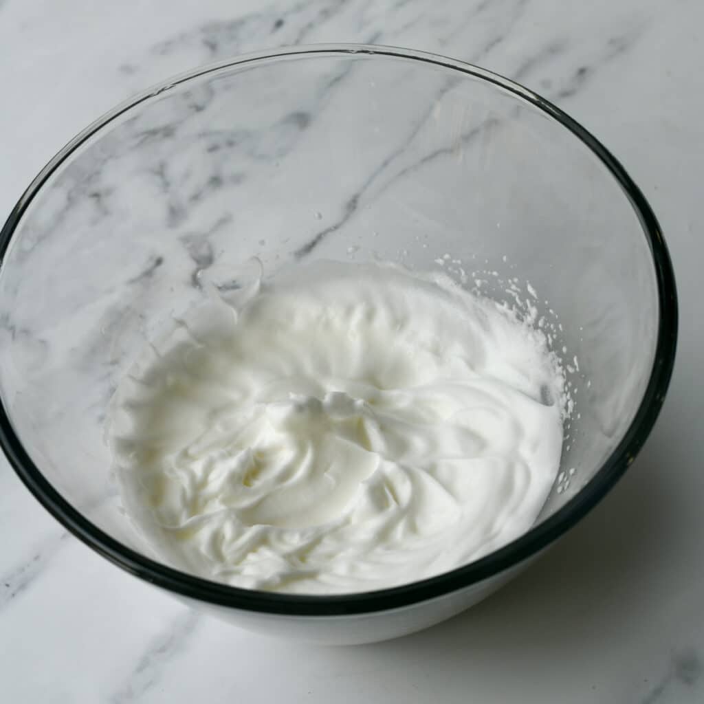 Beating egg whites into a fluffy mixture in a bowl.