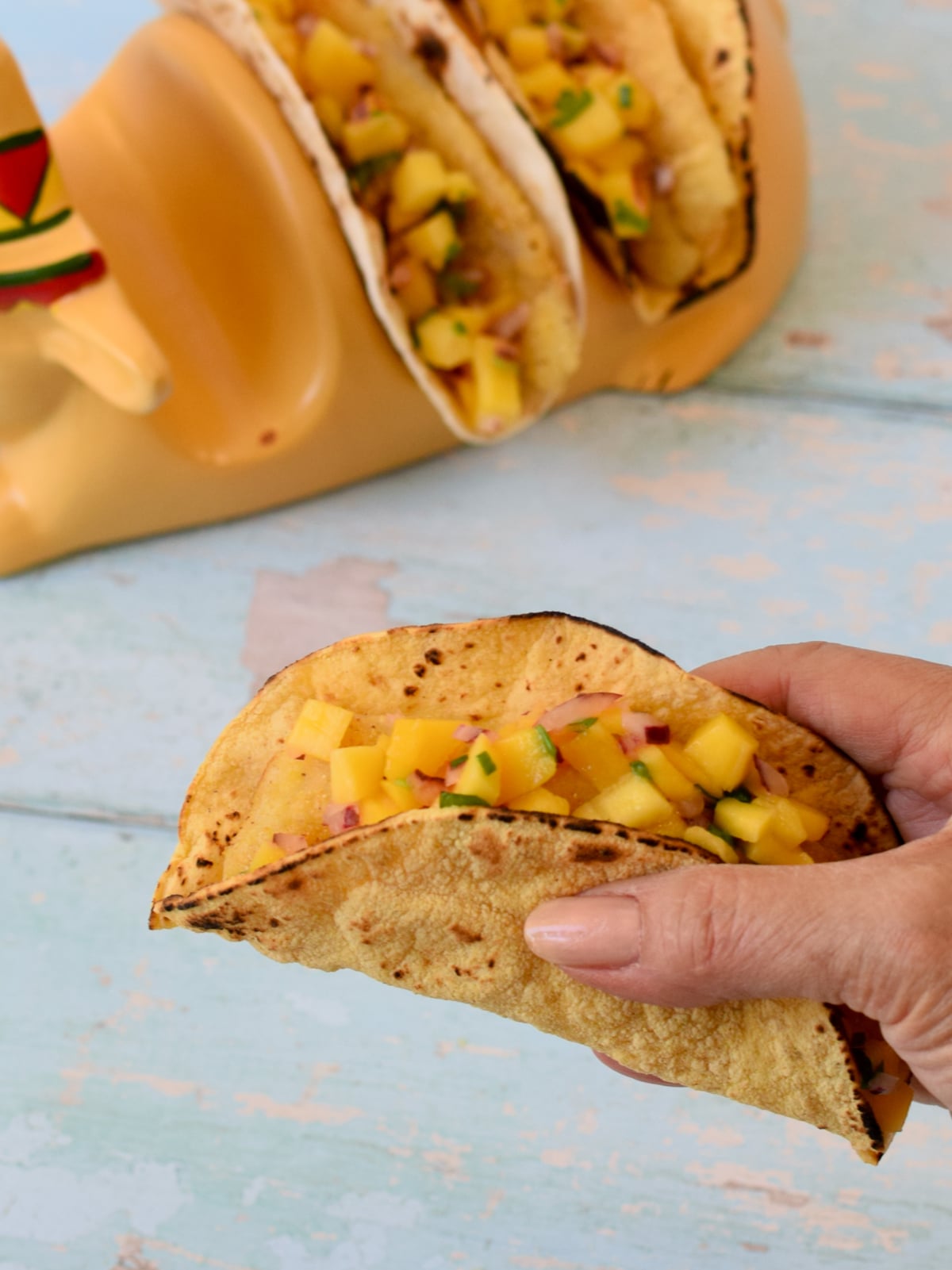 Close up of a hand holding a taco with two other fish tacos with mango salsa in the background.