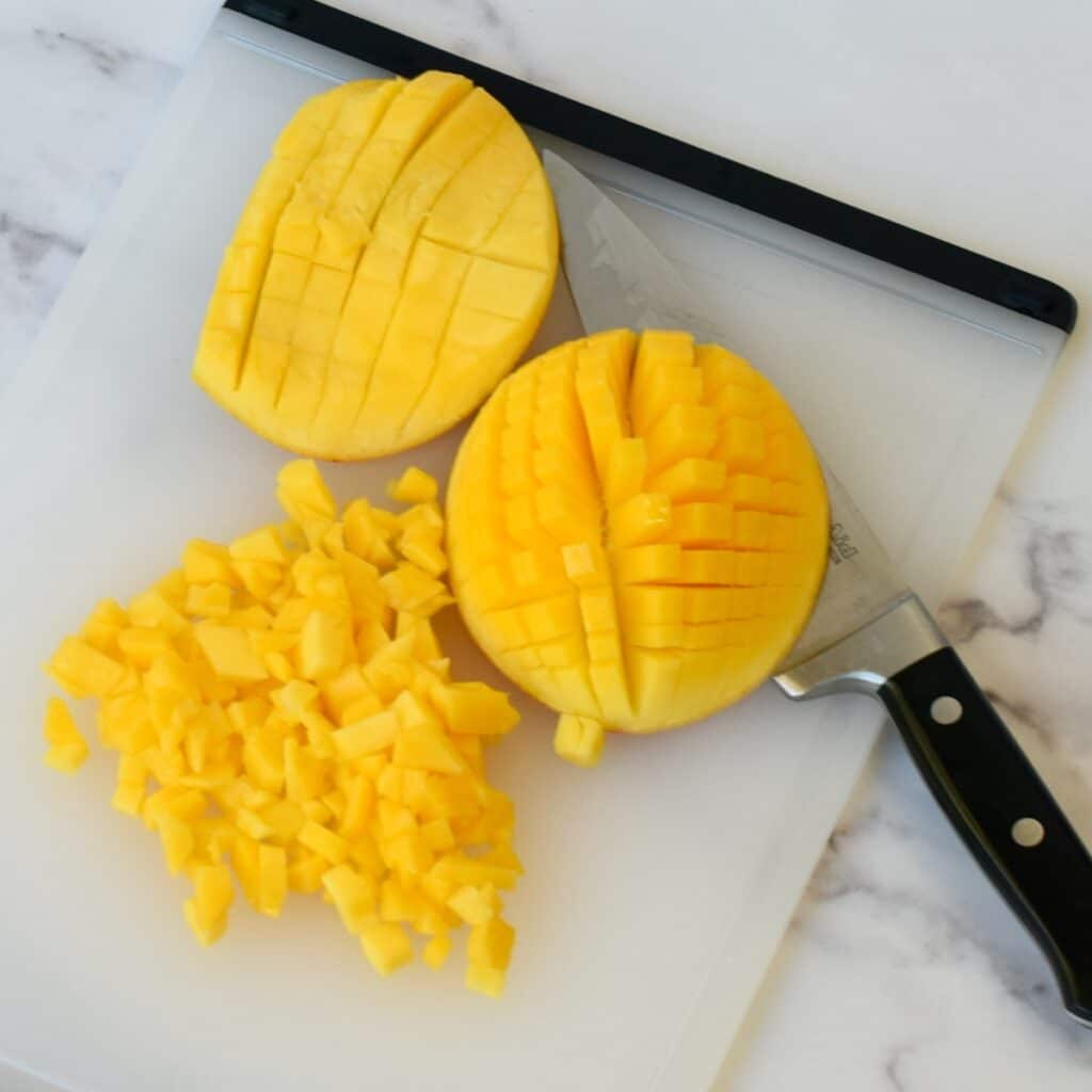Mango halves diced on a cutting board for salsa.
