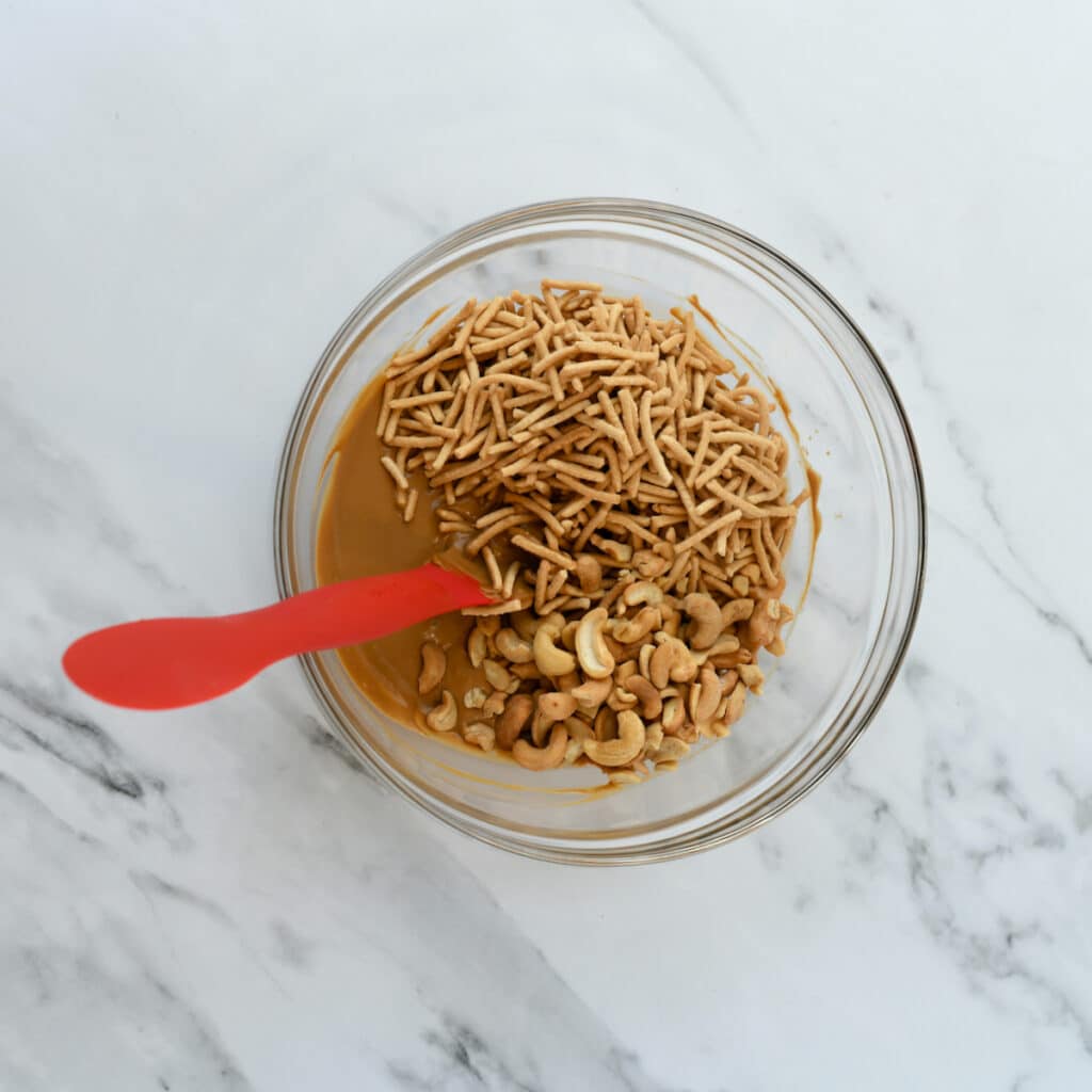 Melted cookie butter, butterscotch chips, chow mein noodles and cashews in a glass bowl.
