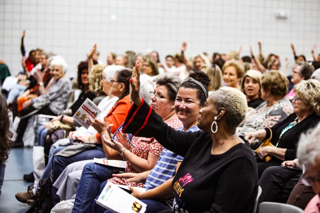 Crowd of women holding up hands smiling. 2023