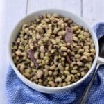 Purple hull peas with bacon and ham in white bowl on blue cloth.