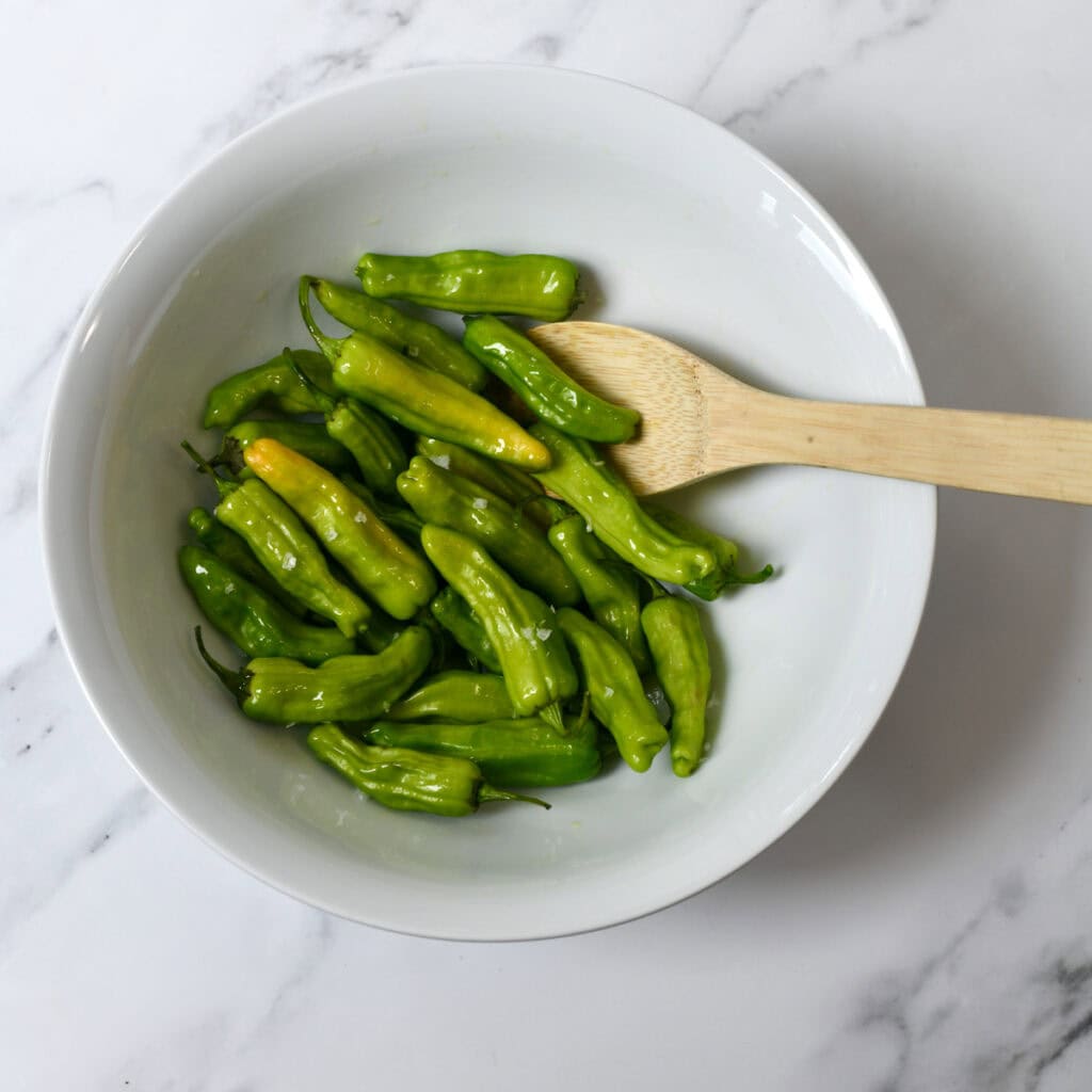 Shishito peppers tossed with olive oil in white bowl.