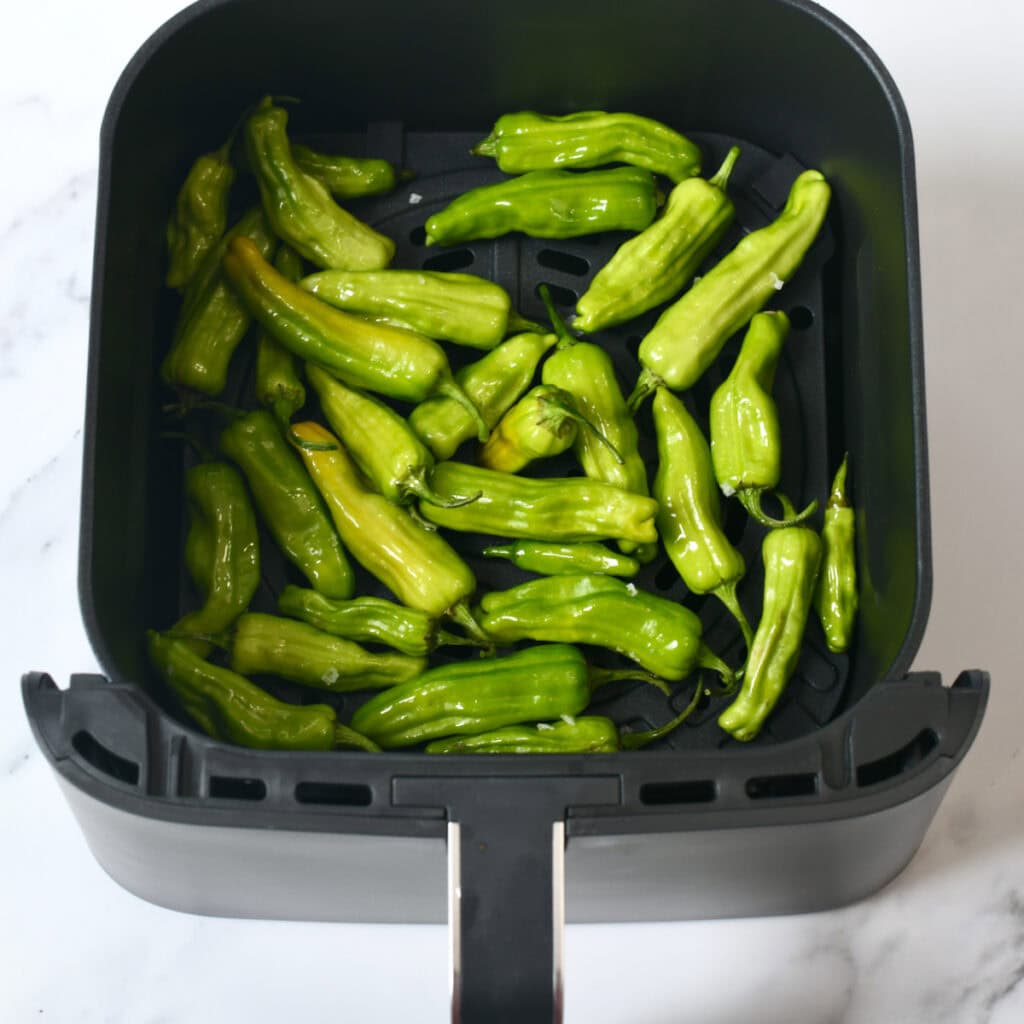 Shishito peppers tossed with olive oil in an air fryer basket.