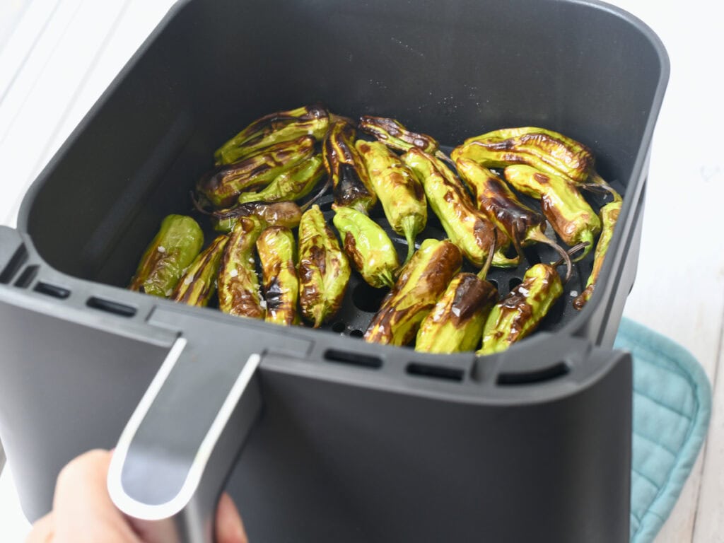Shishito peppers tossed with olive oil roasted in an air fryer basket.
