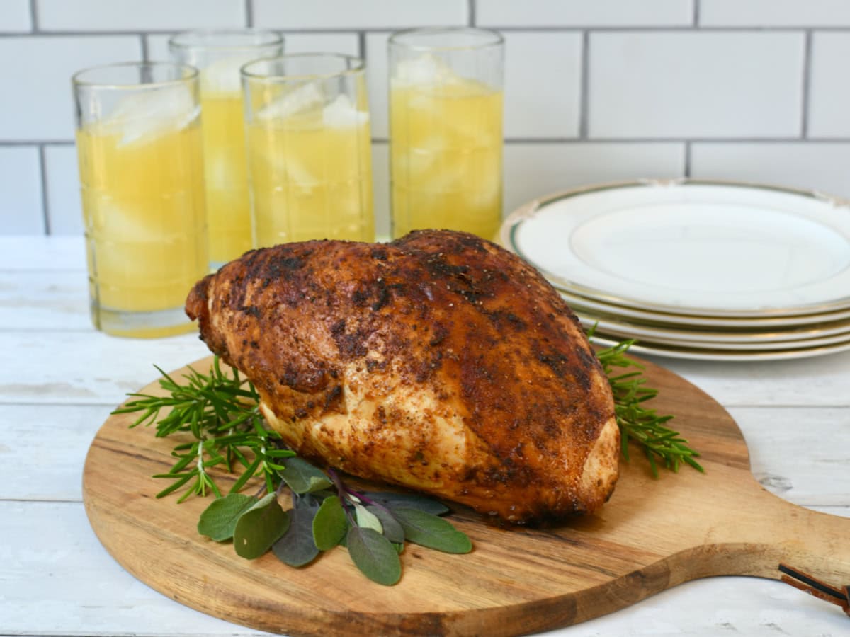 Roasted turkey breast on wooden cutting board with lemonade glasses in background.